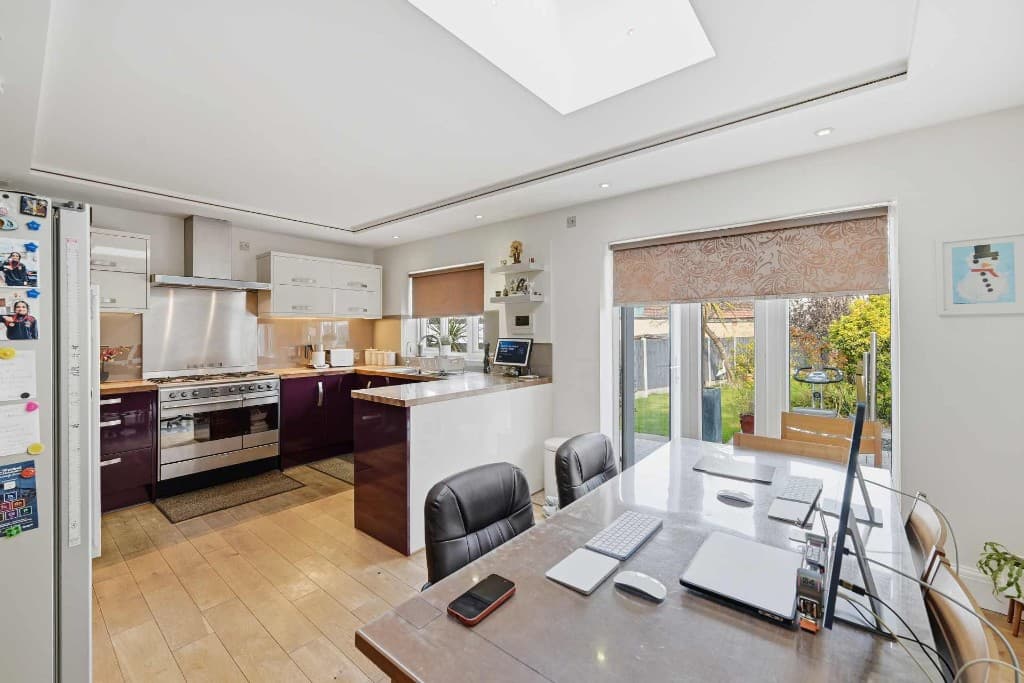 Open-plan kitchen diner with laptops, a phone and clutter on the table and worktops